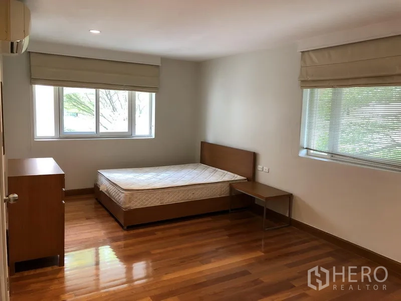 Detached House for rent in Watthana, Bangkok - Large secondary bedroom with corner windows, wood floors and a simple bed.
