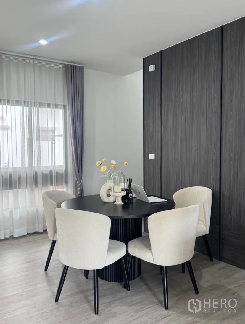 บ้านเดี่ยว for rent or sale in Lat Krabang, Bangkok - มุมรับประทานอาหาร โต๊ะกลมสีดำ เก้าอี้บุนวมสีครีมสี่ตัว ข้างหน้าต่างม่านโปร่ง