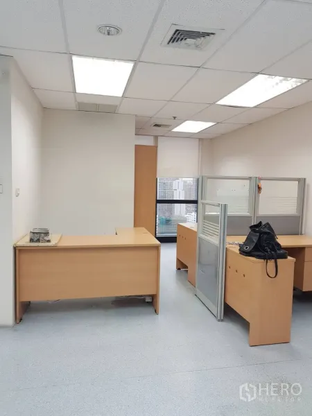 Office Space for rent in Bang Na, Bangkok - Open-plan workspace with light wood desks, cubicles, and bright ceiling lights facing city windows.