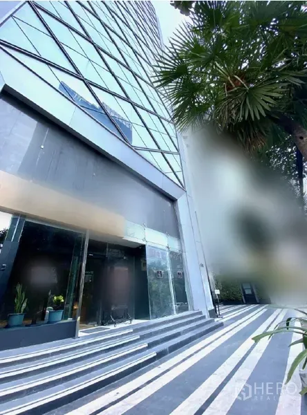 零售空间 出租在Watthana, Bangkok - 高层建筑裙房外观，条纹步道与棕榈树景观。