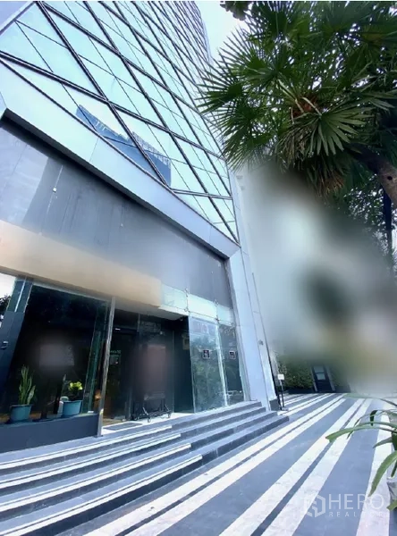 零售空间 出租在Watthana, Bangkok - 高层建筑裙房外观，条纹步道与棕榈树景观。