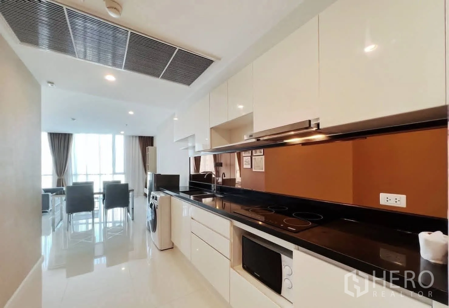 Condominium for rent in Watthana, Bangkok - Galley kitchen with glossy cabinets, electric cooktop, range hood, microwave, fridge, and washing machine.