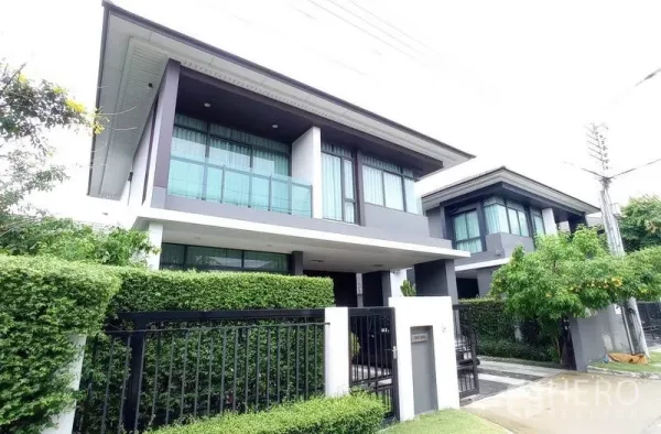 Detached House for rent in Bang Kapi, Bangkok - Angled exterior view showing glass balcony, large windows and manicured hedges.