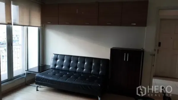 Condominium for rent in Bang Rak, Bangkok - Living room featuring black leather sofa, overhead storage and balcony windows with blinds.