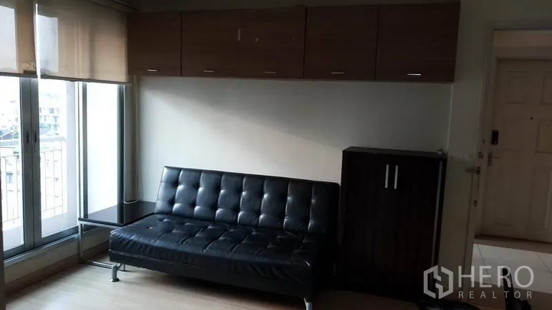 Condominium for rent in Bang Rak, Bangkok - Living room featuring black leather sofa, overhead storage and balcony windows with blinds.