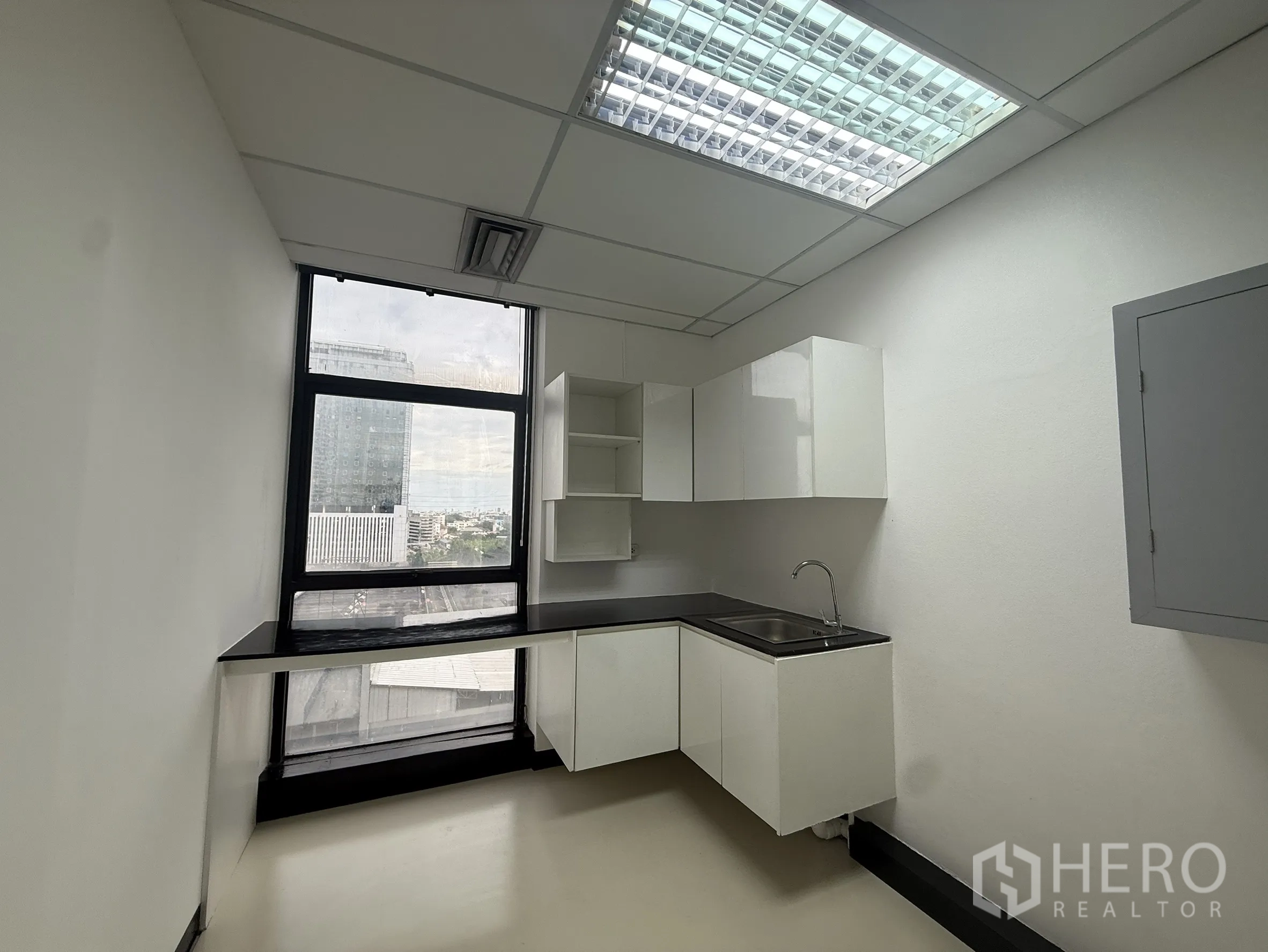 Office Space for rent - Compact office pantry with white cabinetry, sink, long countertop, and a tall window overlooking the city.