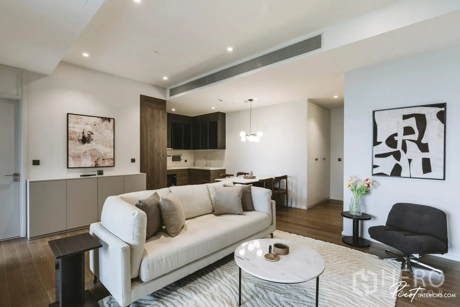 Condominium for rent in Pathum Wan, Bangkok - Spacious lounge with light sofa, round coffee table, artwork, and kitchen-dining zone beyond.
