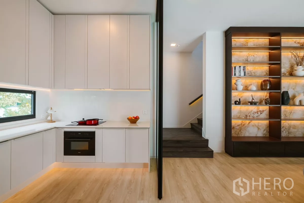 บ้าน ให้เช่าหรือขายในSaphan Sung, Bangkok - ครัวรูปตัวแอลโทนสว่าง เตาอบบิวท์อิน หน้าต่าง และชั้นโชว์ใกล้บันได