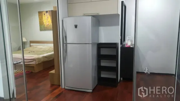 Condominium for rent in Watthana, Bangkok - Compact pantry area with full-size refrigerator and cabinets, hardwood floors, and a bedroom visible through glass doors.