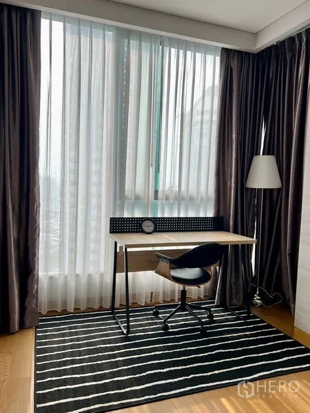 คอนโด ให้เช่า - มุมทำงานริมหน้าต่างสูงจรดเพดาน มีโต๊ะและเก้าอี้ พร้อมผ้าม่านโปร่งรับแสงเมือง