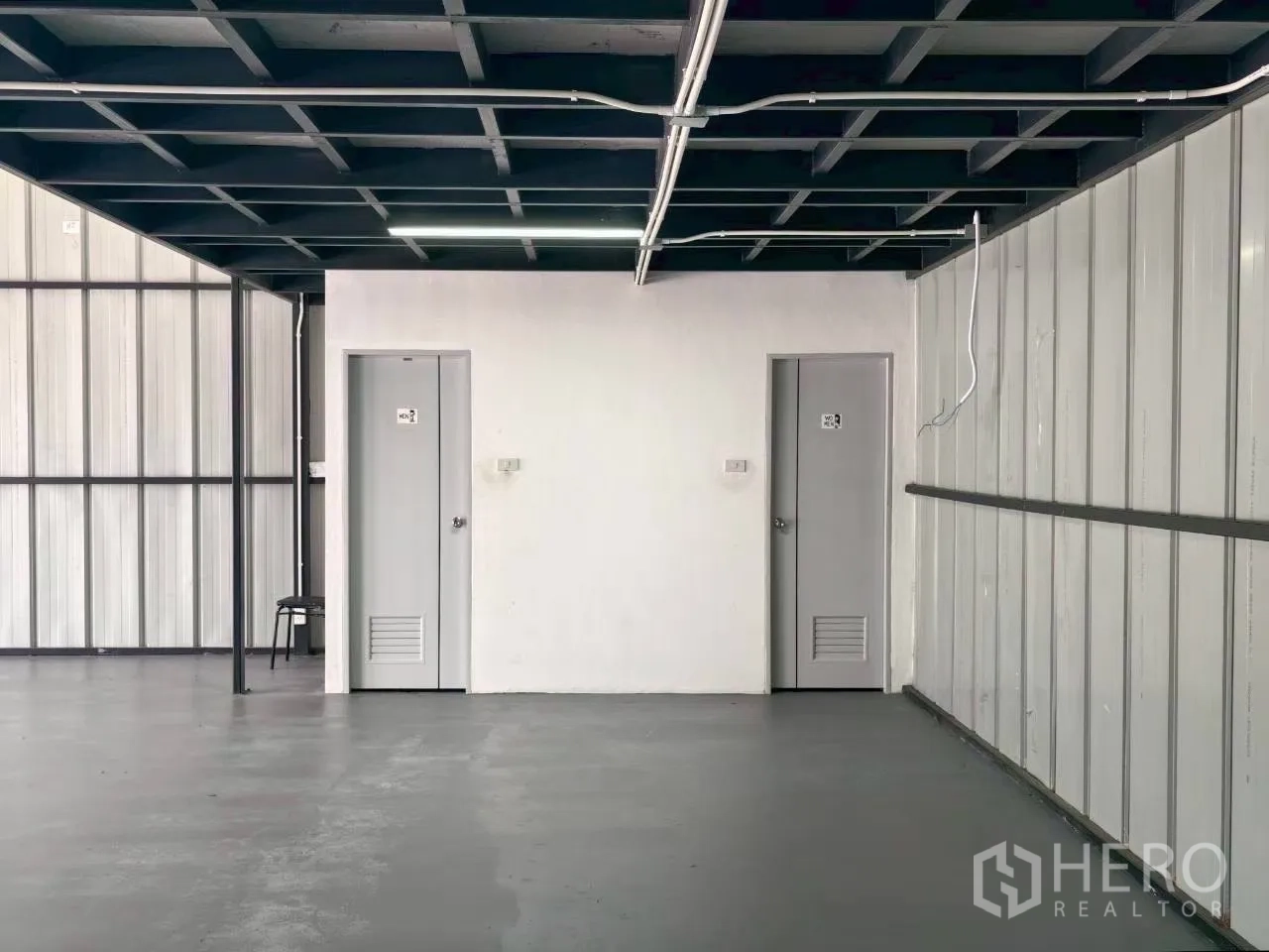 Warehouse for rent in Suan Luang, Bangkok - Close-up of two gray service doors set in a white wall beneath the mezzanine level.
