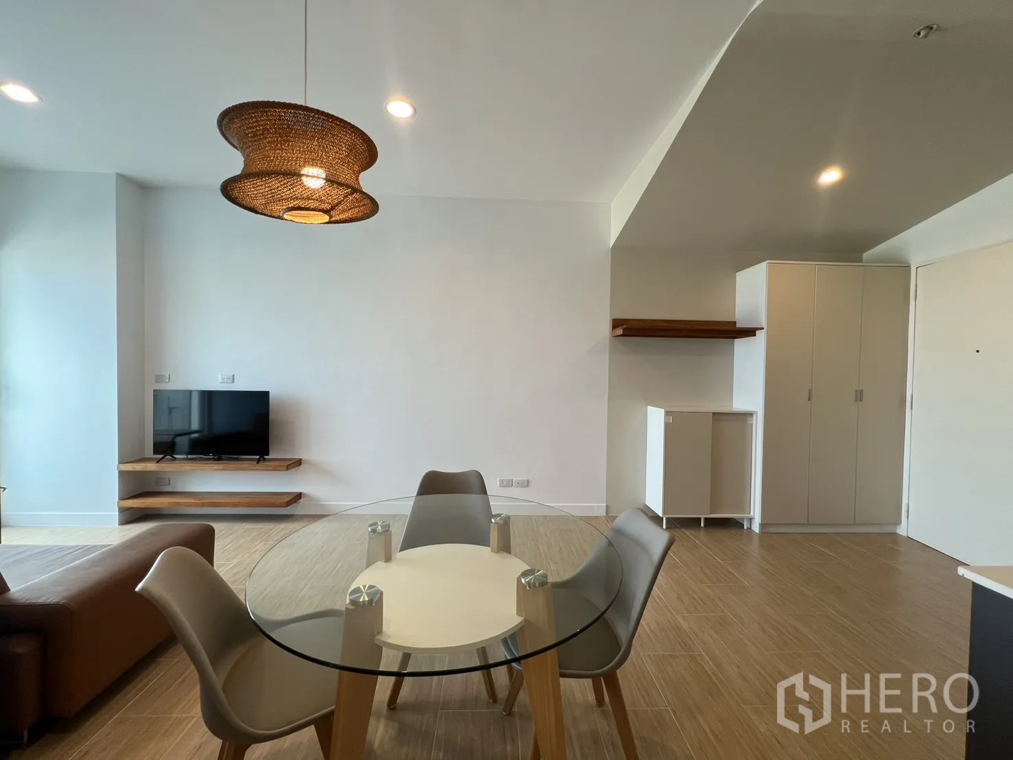 Condominium for rent in Bang Kapi, Bangkok - Wall-mounted TV on floating wooden shelves opposite a glass dining table.