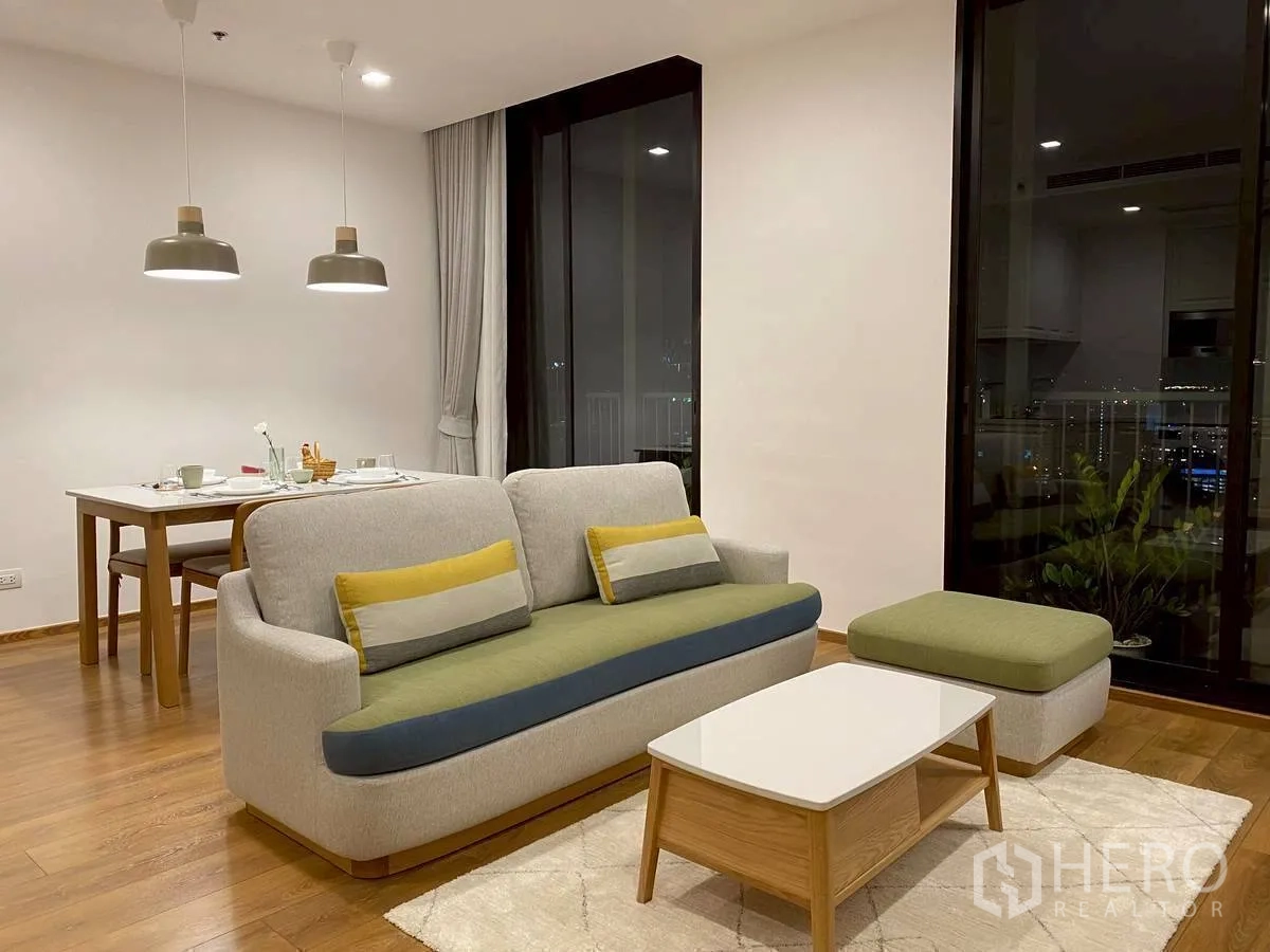 Condominium for rent in Watthana, Bangkok - Night view of the living-dining space with pendant lights and floor-to-ceiling glass.