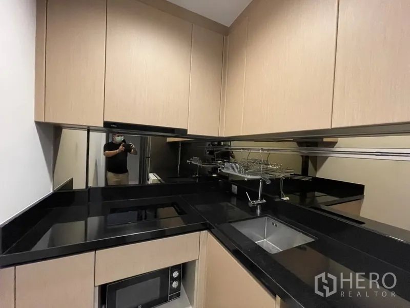 公寓 出租在Watthana, Bangkok - U型厨房，黑色石材台面与浅木橱柜。
