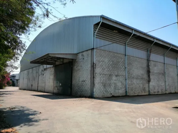 Warehouse for rent in Chaloem Phra Kiat, Saraburi - Large corrugated metal and block-built warehouse exterior with wide driveway and sliding steel door in Chaloem Phra Kiat, Saraburi.