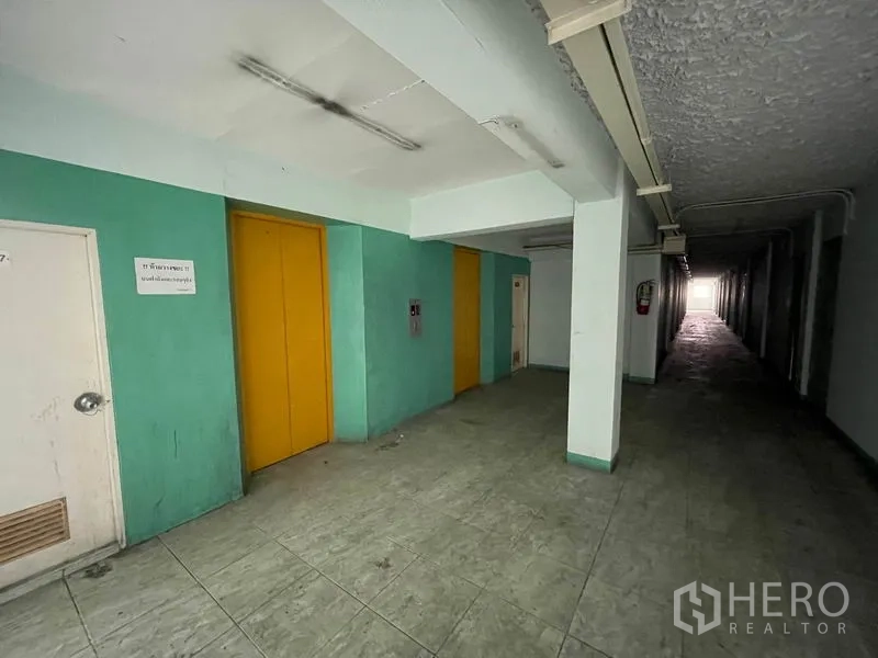 Apartment for sale in Mueang Samut Prakan, Samut Prakan - Ground-floor corridor with two yellow elevator doors in an older apartment building.