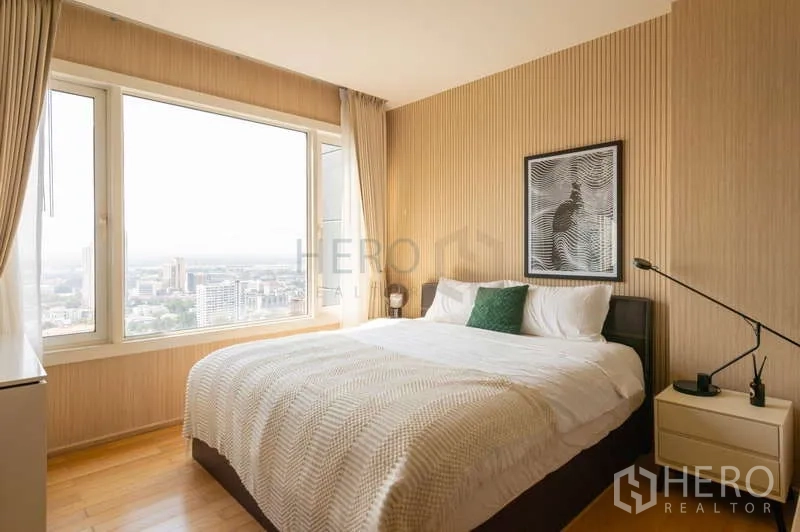Condominium for sale in Khlong Toei, Bangkok - Bedroom with large window overlooking the city and warm wood wall panels.
