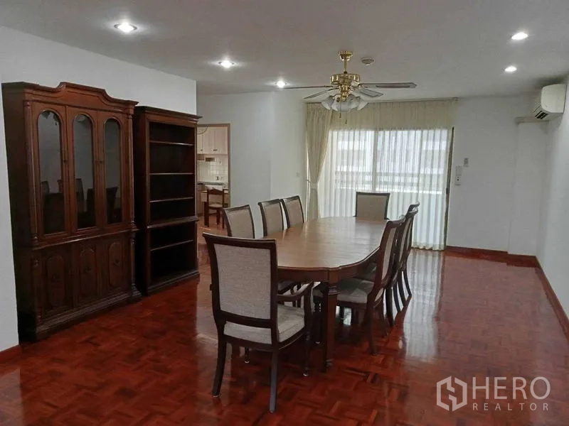 Condominium for rent in Watthana, Bangkok - Dining area with eight-seat wooden table, display cabinet and sheer-curtained balcony doors.