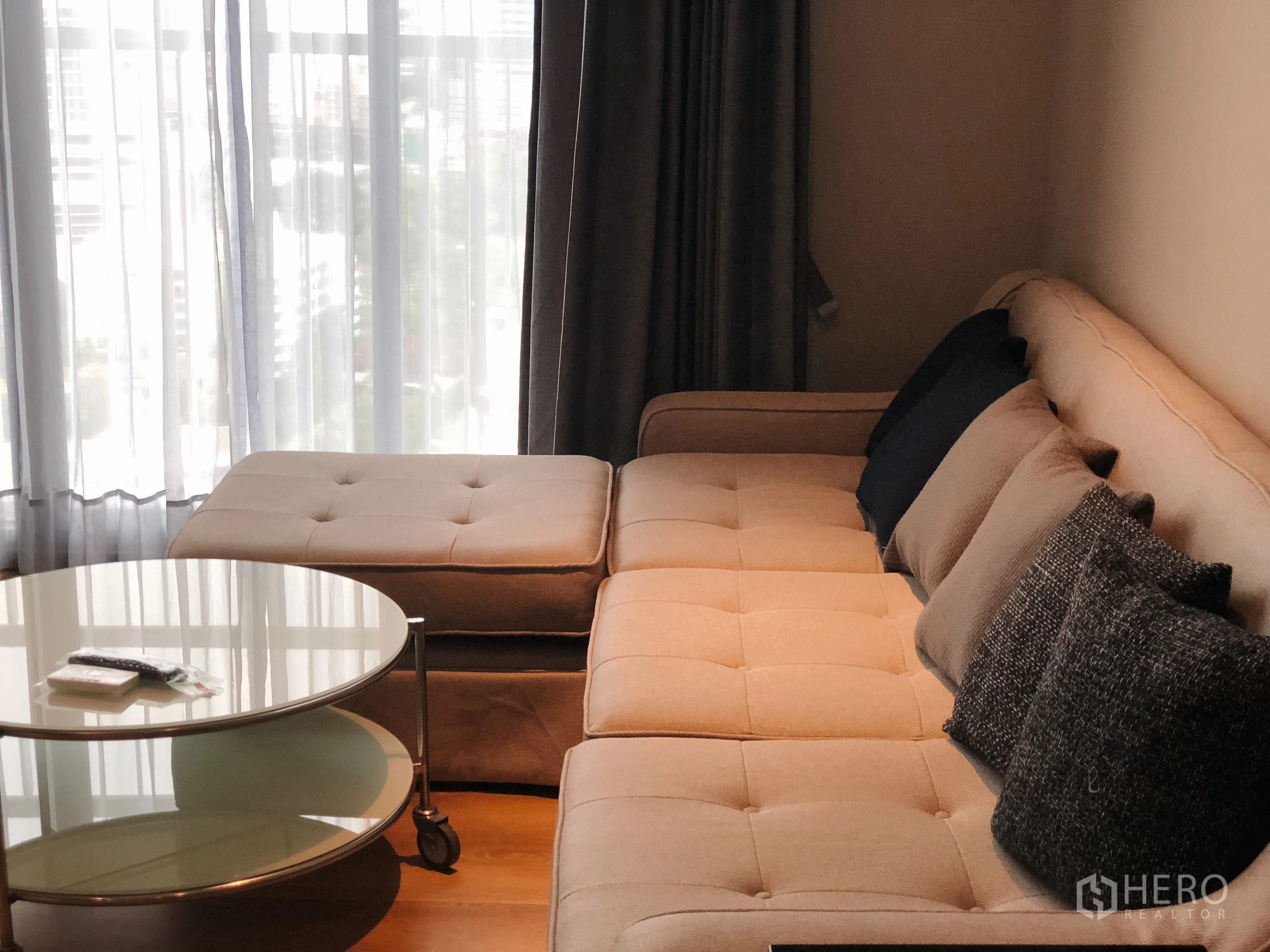 คอนโด ให้เช่าในKhlong Toei, Bangkok - โซฟาสีครีมพร้อมออตโตมาน โต๊ะกลางกระจกข้างหน้าต่างสูง
