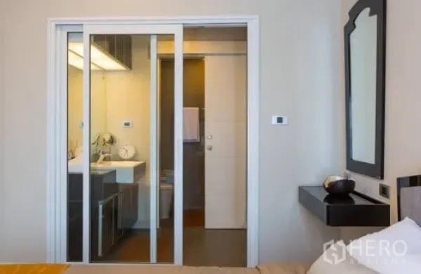 公寓 出租在Khlong Toei, Bangkok - 卧室望向浴室的玻璃推拉门与现代台上方形洗手盆。