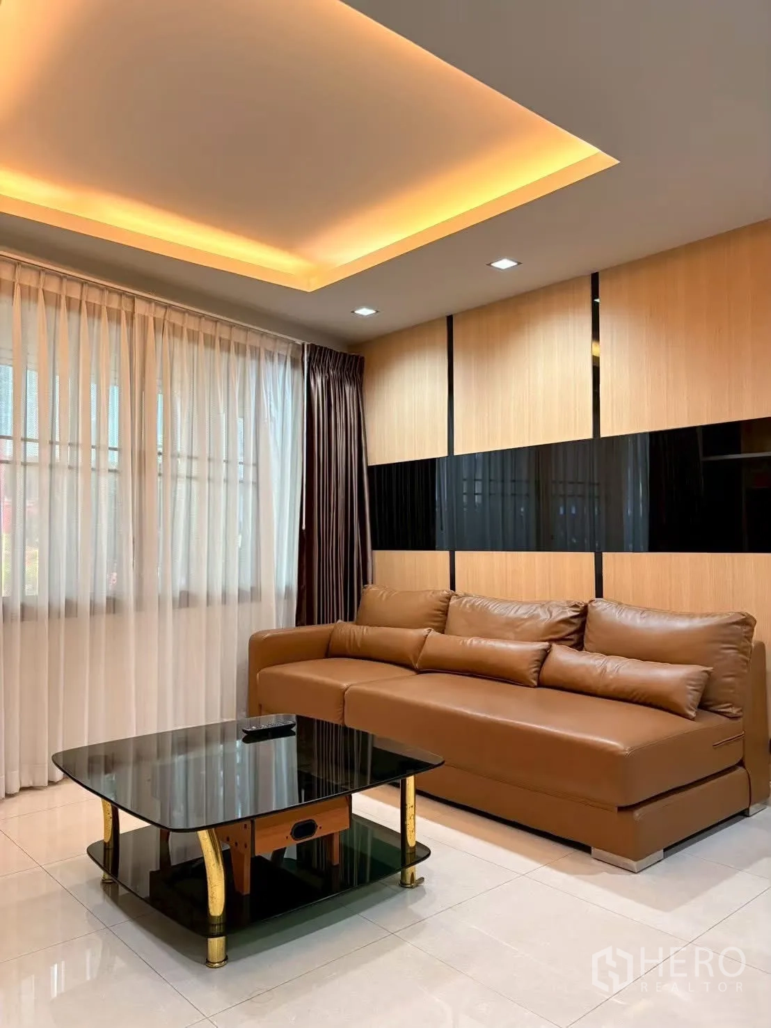 联排别墅 for rent in Pathum Wan, Bangkok - 客厅配棕色皮沙发、玻璃茶几与暖色灯带吊顶。