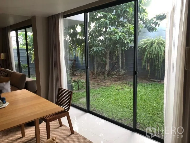 Detached House for rent or sale in Huai Khwang, Bangkok - Sliding glass doors open to a private garden with lawn, trees and a fenced backdrop.