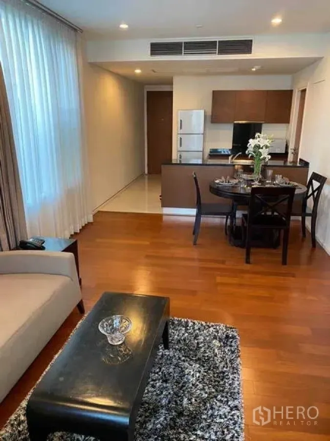 Condominium for rent in Watthana, Bangkok - Open-plan living and dining area with round table, sofa, rug, and kitchen in the background.