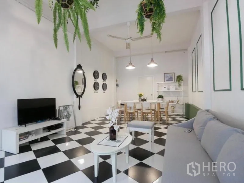 Townhouse for rent in Khlong Toei, Bangkok - Bright open-plan living and dining area with black-and-white checkerboard floor, hanging ferns, TV console and a wooden dining set.