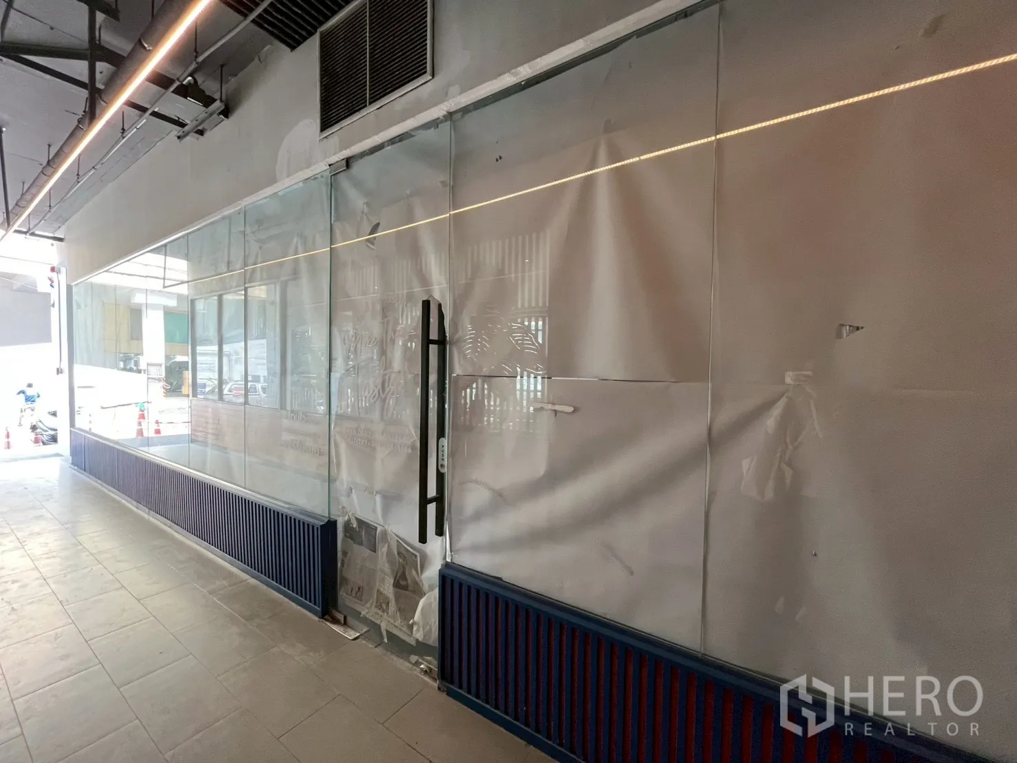 Retail Space for rent in Watthana, Bangkok - Extended floor-to-ceiling glass shopfront with door handle, wide interior passageway, tiled floor, and exposed ceiling with linear lighting and air vent.