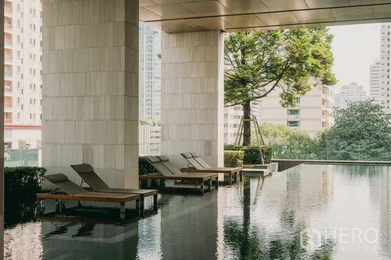 Condominium for rent or sale in Watthana, Bangkok - Covered infinity pool with sun loungers and greenery in condominium facilities.