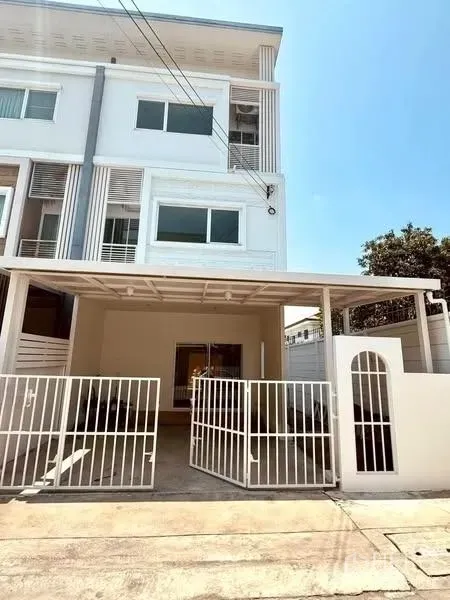 Townhouse for rent in Suan Luang, Bangkok - Modern three-storey townhouse facade with covered carport and white metal gate.