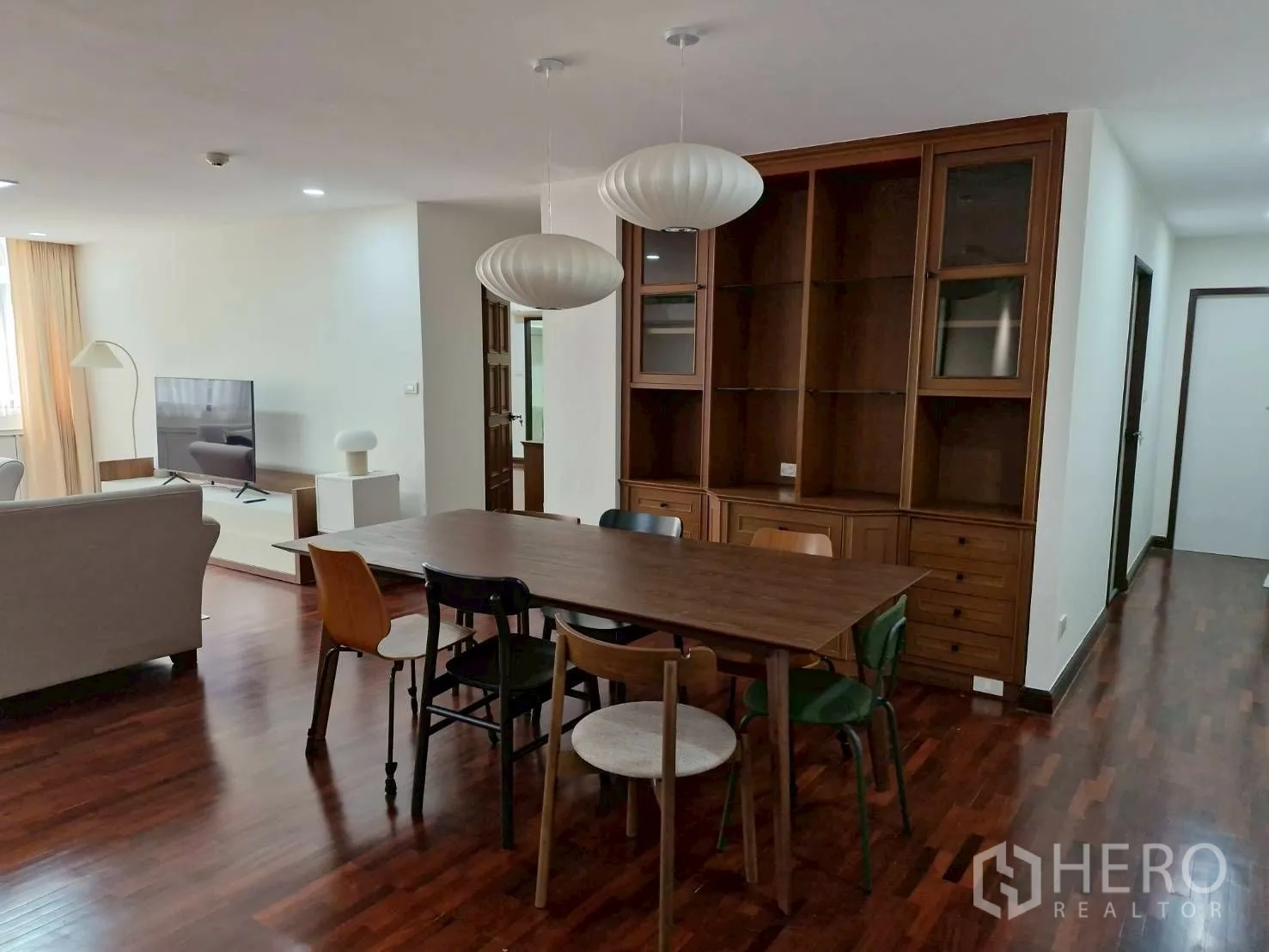 Condominium for rent in Khlong Toei, Bangkok - Dining area with wooden table, mixed chairs, built-in shelving and pendant lights.