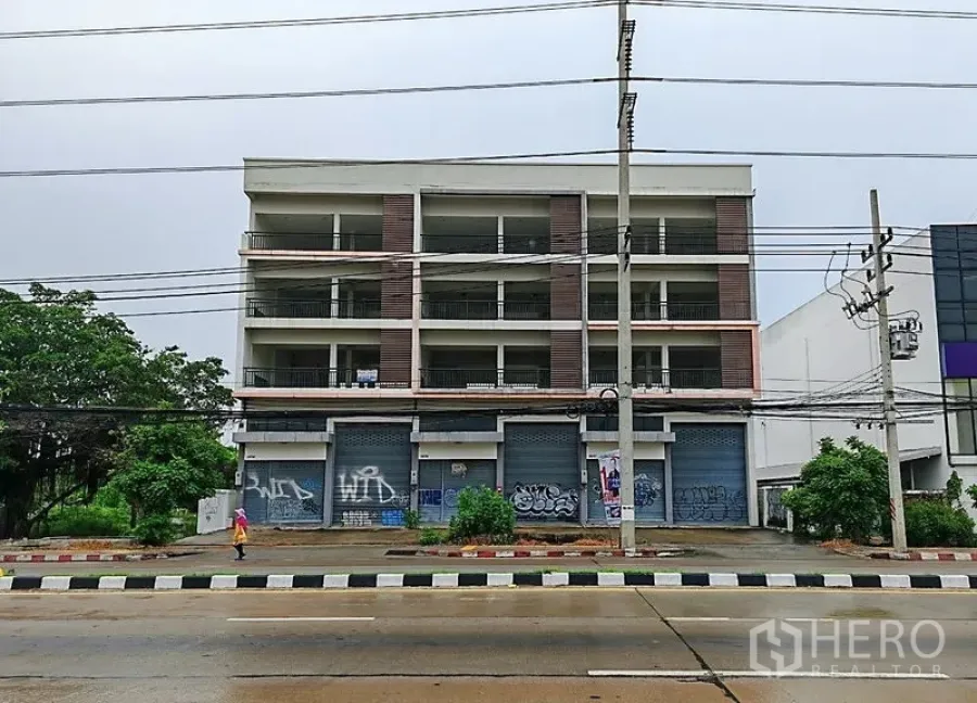 Home Office for rent or sale in Lam Luk Ka, Pathum Thani - Street view of the property facade and sidewalk along a busy thoroughfare.