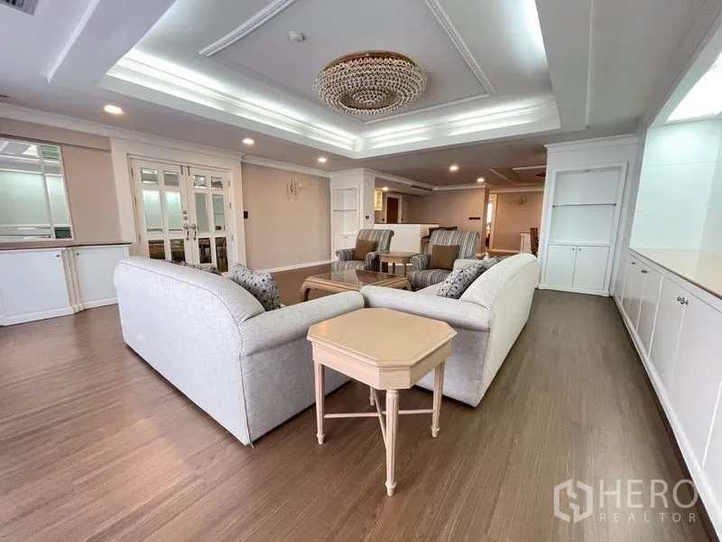 Condominium for rent in Watthana, Bangkok - Spacious living room with coffered ceiling, chandelier, wood floors, and a sofa set.
