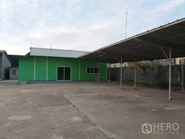 คลังสินค้า ให้เช่าในKhlong Sam Wa, Bangkok - อาคารสำนักงานสีเขียวพร้อมประตูกระจกบานเลื่อน ข้างกันสาดจอดรถและลานคอนกรีต