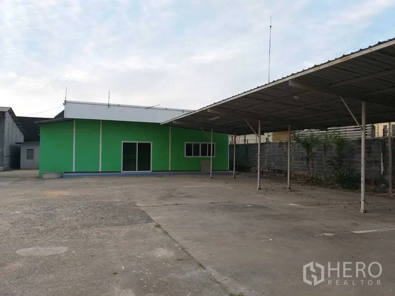 คลังสินค้า ให้เช่าในKhlong Sam Wa, Bangkok - อาคารสำนักงานสีเขียวพร้อมประตูกระจกบานเลื่อน ข้างกันสาดจอดรถและลานคอนกรีต