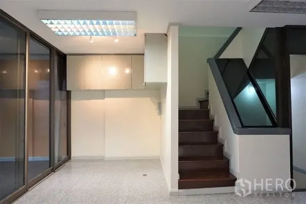 Home Office for rent in Khlong Toei, Bangkok - Bright home office interior with wood staircase, glass balustrade, wall cabinets, and sliding glass doors.