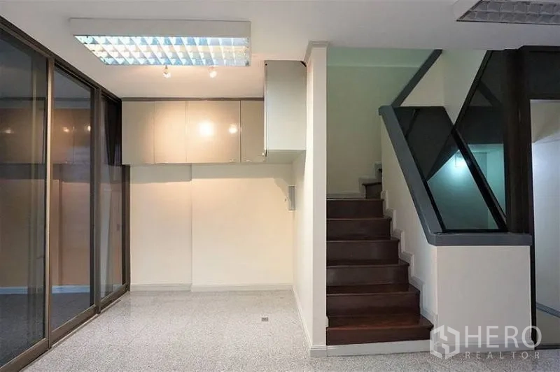 Home Office for rent in Khlong Toei, Bangkok - Bright home office interior with wood staircase, glass balustrade, wall cabinets, and sliding glass doors.