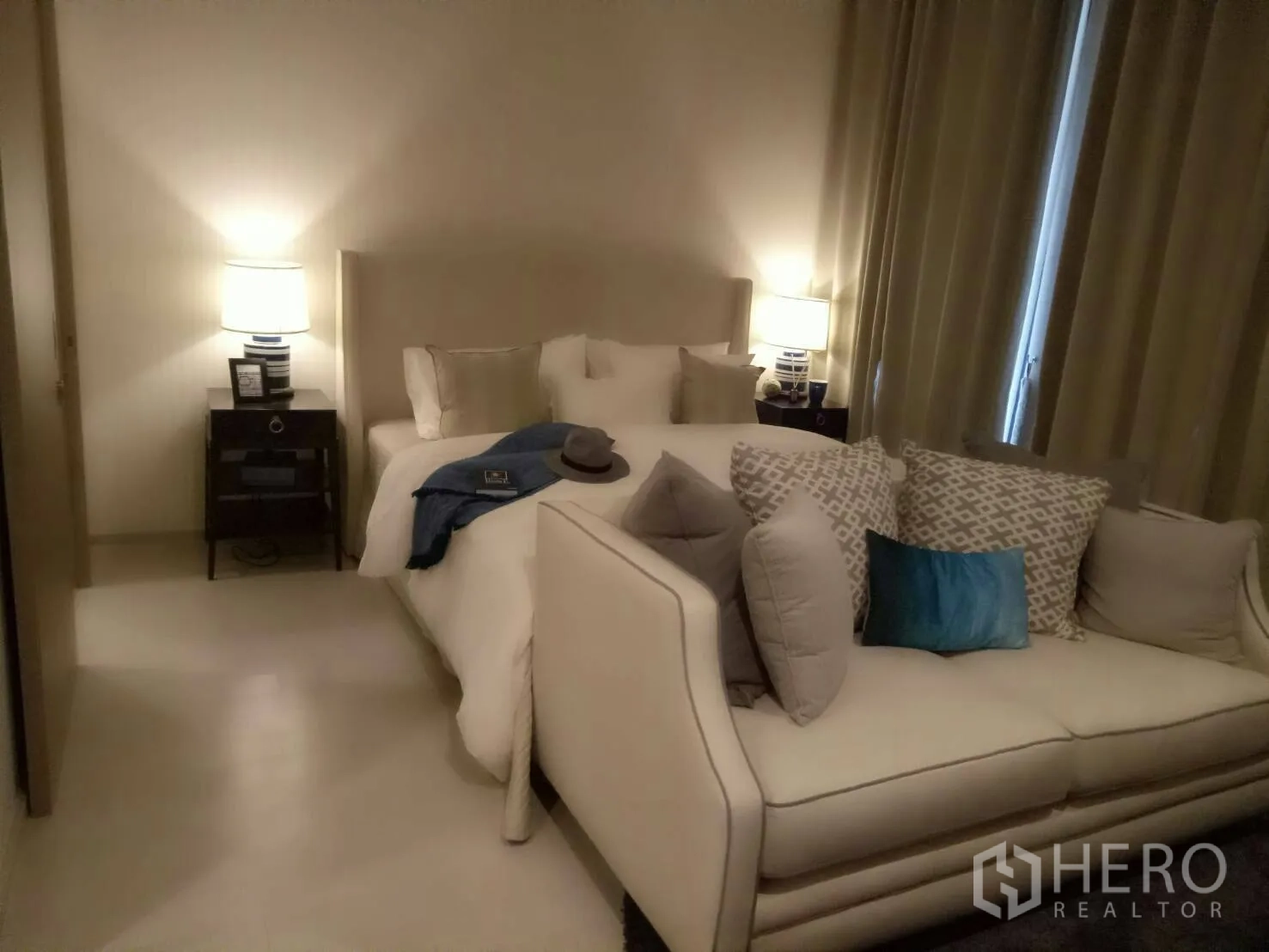 Condominium for rent or sale in Pathum Wan, Bangkok - Cozy bedroom with a plush sofa, bedside tables with lamps, and floor-length curtains in neutral tones.