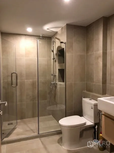 Condominium for rent or sale in Yan Nawa, Bangkok - Modern bathroom with glass-enclosed shower, rain showerhead, and neutral tiles.