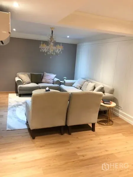 Shophouse for rent or sale in Chatuchak, Bangkok - Cozy living area with L-shaped sofas, chandelier and wood flooring.
