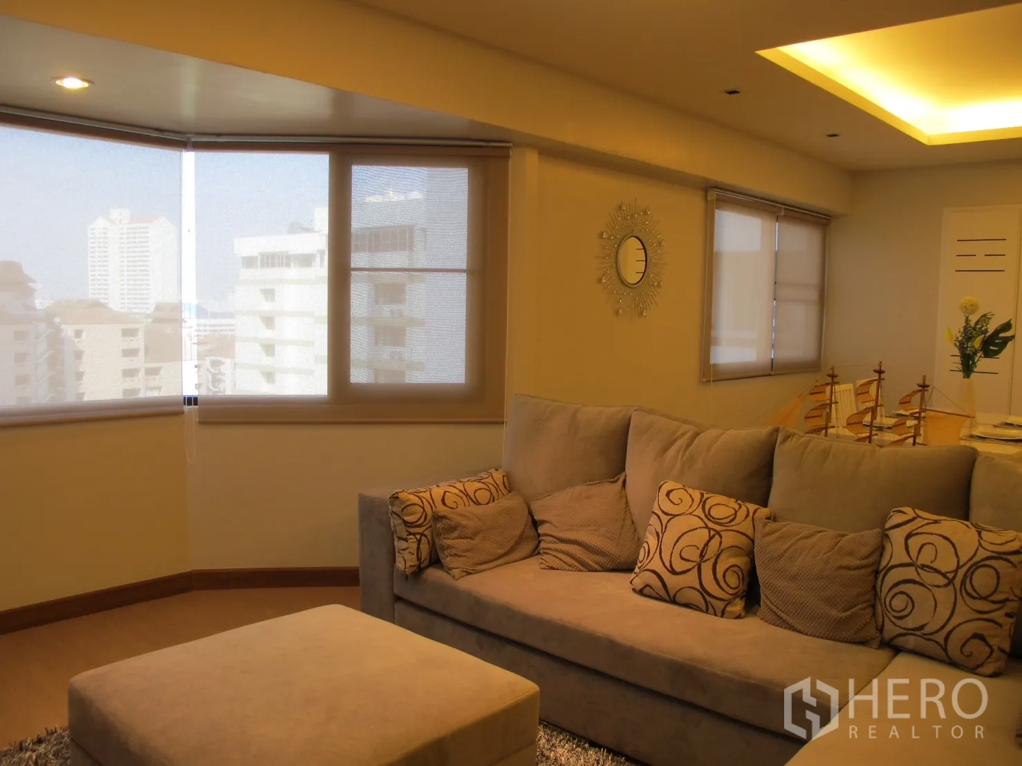 Condominium for rent in Watthana, Bangkok - Bright living room with sectional sofa, ottoman and bay windows facing the city.