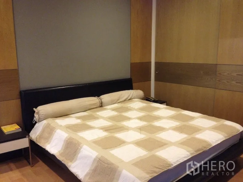 Condominium for rent in Khlong Toei, Bangkok - Bedroom with king-size bed, wood-paneled accent walls and bedside tables.