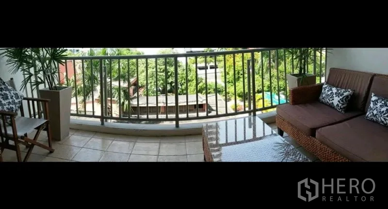 公寓 出租在Khlong Toei, Bangkok - 宽阔阳台配藤编沙发与茶几，栏杆外是绿意与住户泳池景观。