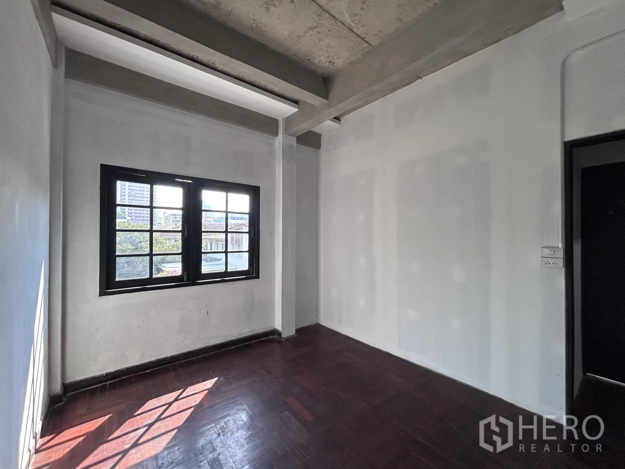 家庭办公室 for rent or sale in Watthana, Bangkok - 房间带裸露混凝土梁、木地板与单扇窗。
