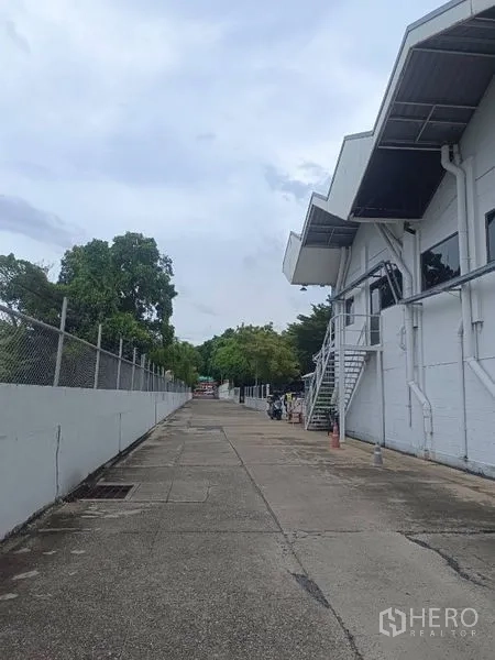 货栈 出租在Lam Luk Ka, Pathum Thani - 仓库侧面长通道，围栏与树木成行，适合卡车通行。