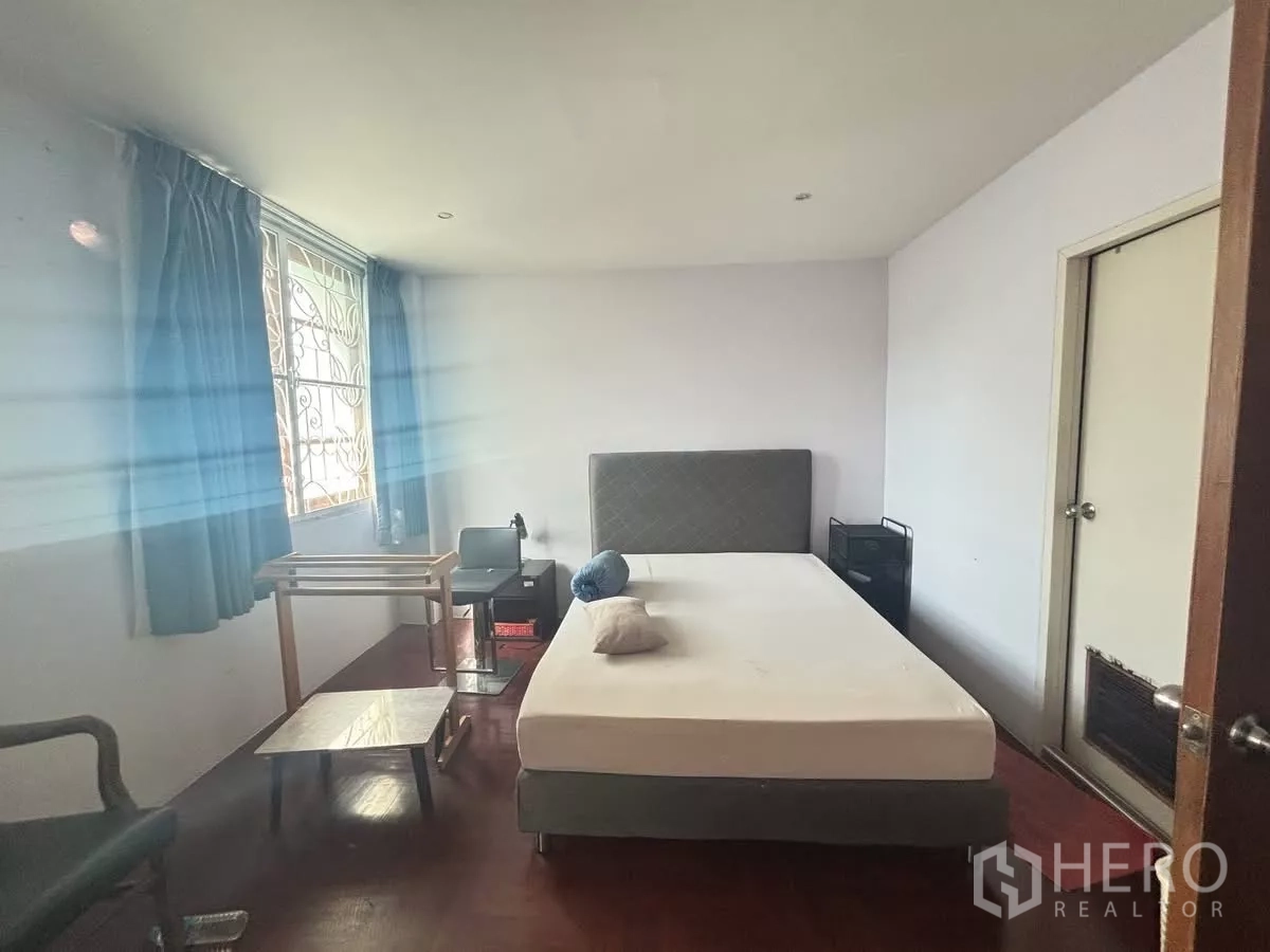 店屋 出租在Watthana, Bangkok - 简洁卧室，带窗与蓝色窗帘，木地板配双人床。