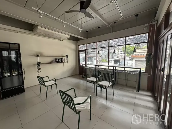 零售空间 出租在Watthana, Bangkok - 明亮座位区，整面落地窗，吧台与高脚椅，瓷砖地面和墙面置物架。