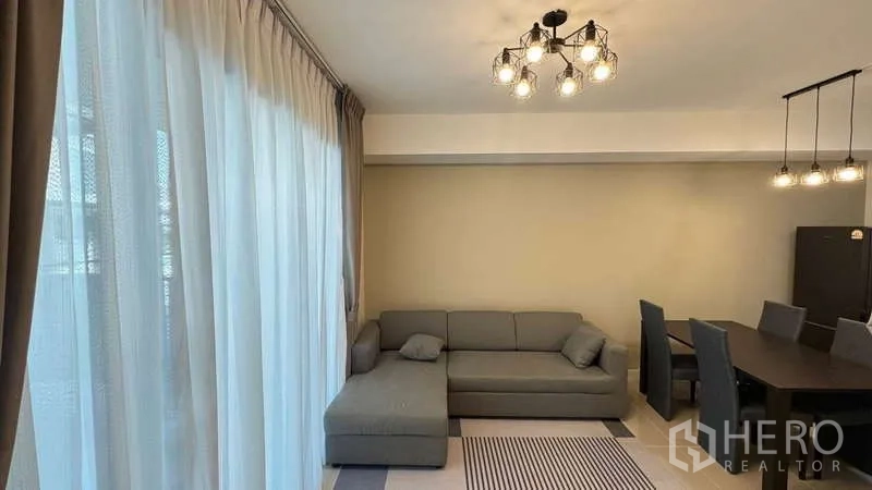 Townhouse for rent in Bang Phli, Samut Prakan - Living area with L-shaped sofa, rug and chandelier next to full-height windows.