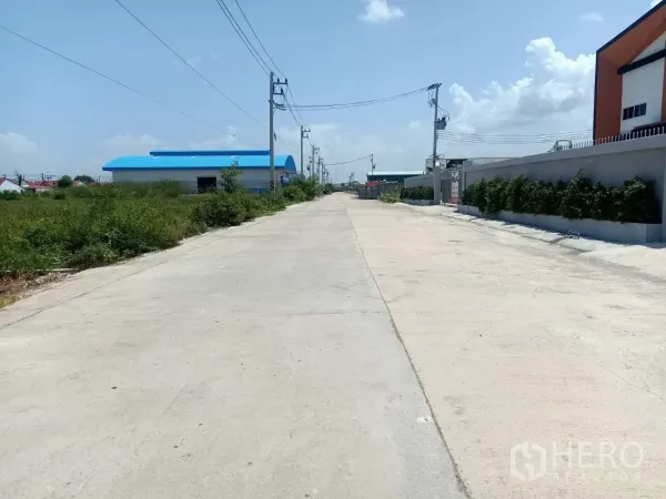 工厂 出租或出售在Mueang Samut Sakhon, Samut Sakhon - 工厂前的宽阔工业混凝土道路，沿线电线杆与绿化围墙。